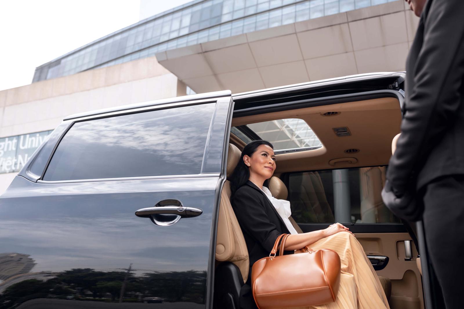 Chauffeur in a dark suit holding open the rear door of a black sedan